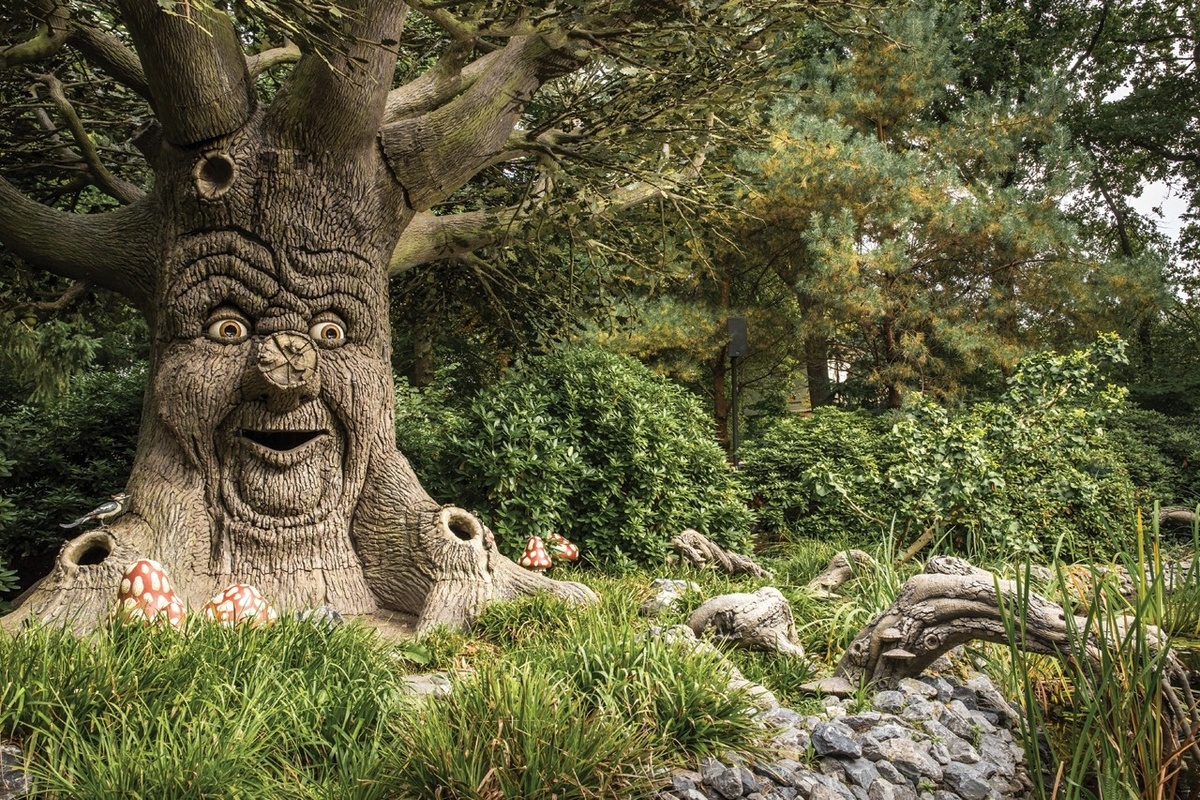 Smiling tree with a face, surrounded by foliage and toadstools in the Fairytale Forest at Efteling.