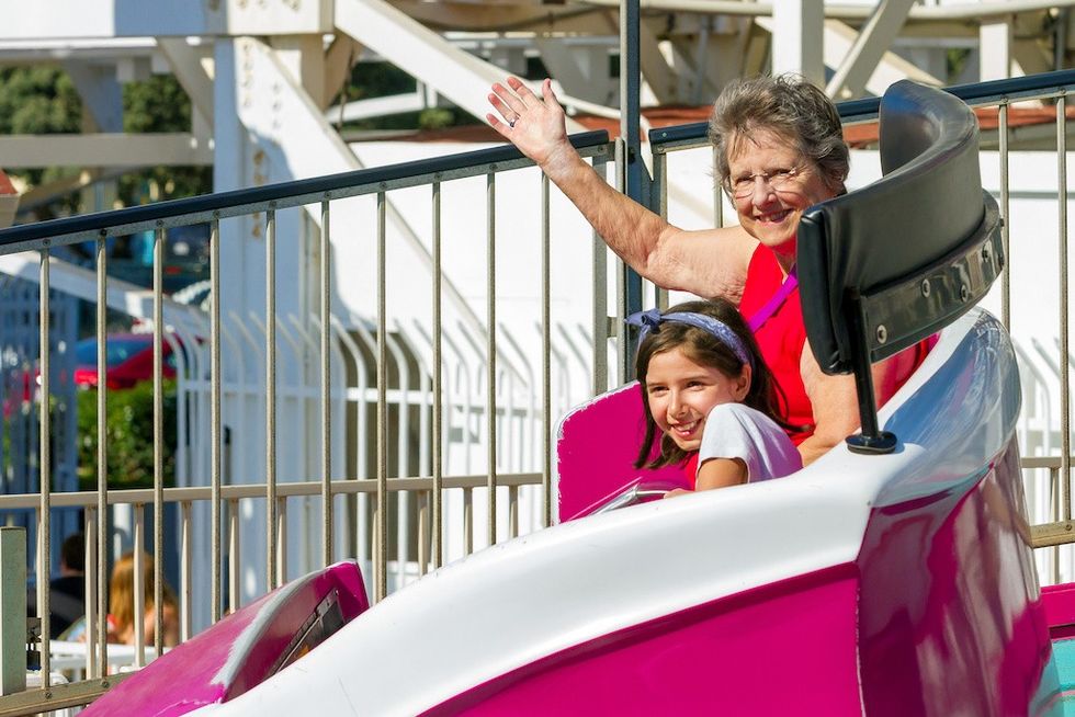 Smiling woman and child on amusement ride; woman waves, child looks excited.