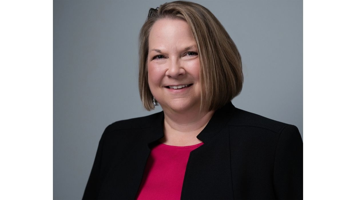 Smiling woman, AZA's Melissa Howerton, in a black blazer and pink top, against a gray background.