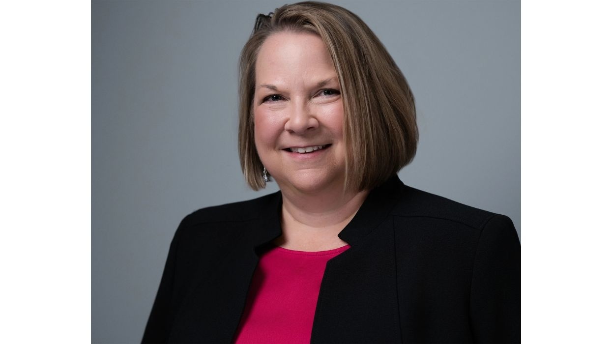Smiling woman, AZA's Melissa Howerton, in a black blazer and pink top, against a gray background.
