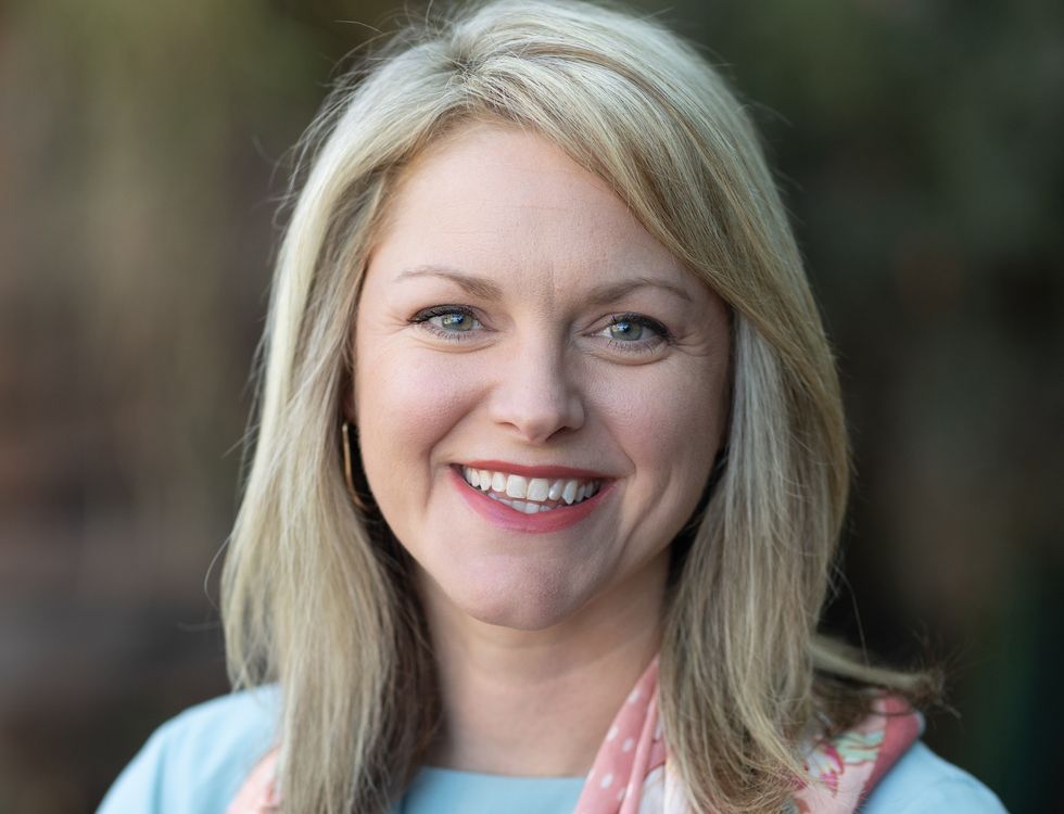 Smiling woman called Jennifer Driban with blonde hair and a floral scarf in an outdoor setting.