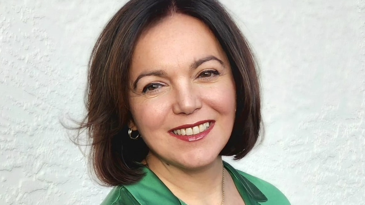 Smiling woman called Una de Boer with short brown hair in a green top against a textured white background.