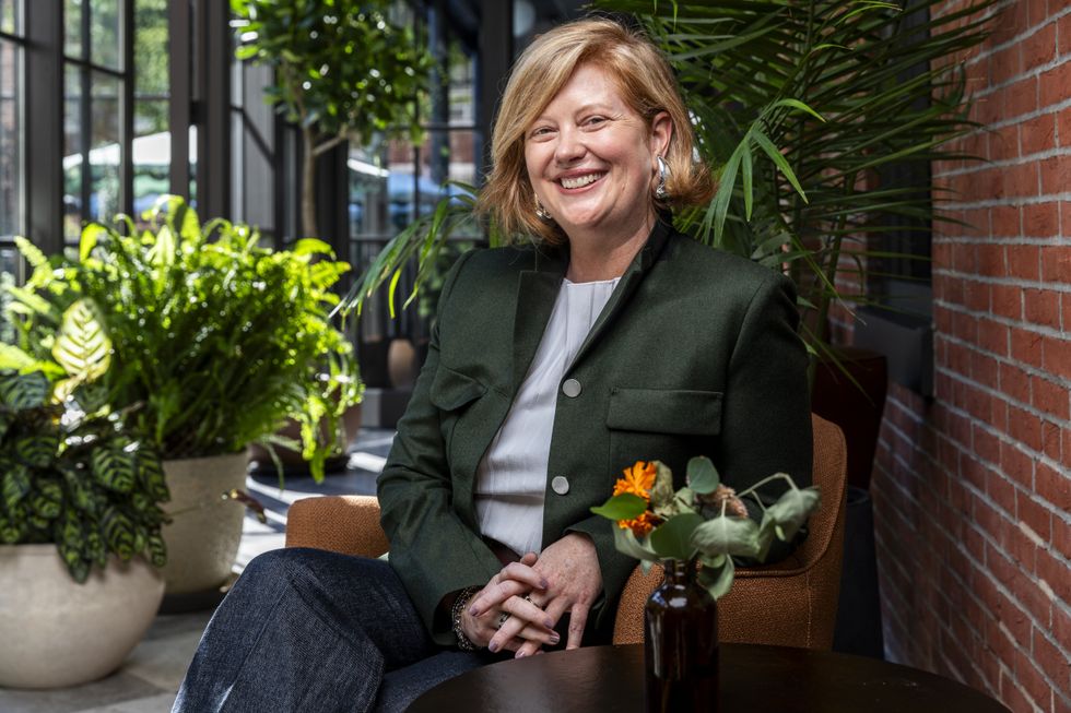Smiling woman in a blazer named Abby Bysshe, sitting in a bright room with plants.