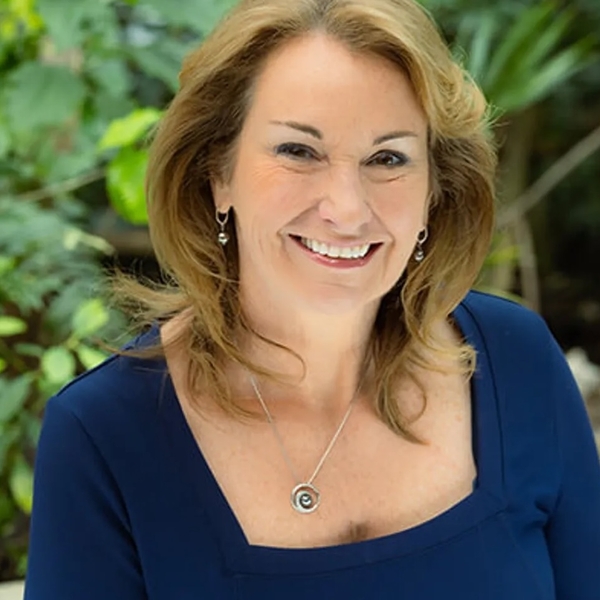 Smiling woman in a blue dress with greenery in the background.