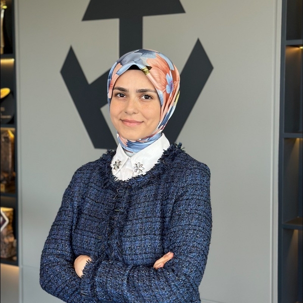 Smiling woman in a floral headscarf and blue jacket, standing with arms crossed.