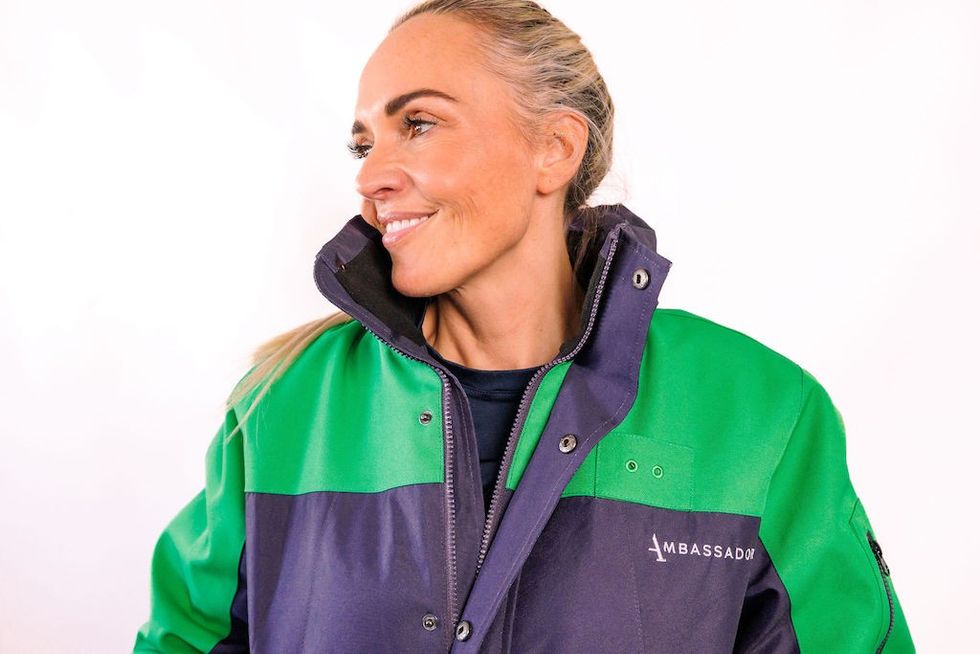 Smiling woman in a green and navy jacket with "AMBASSADOR" text, looking to the side.
