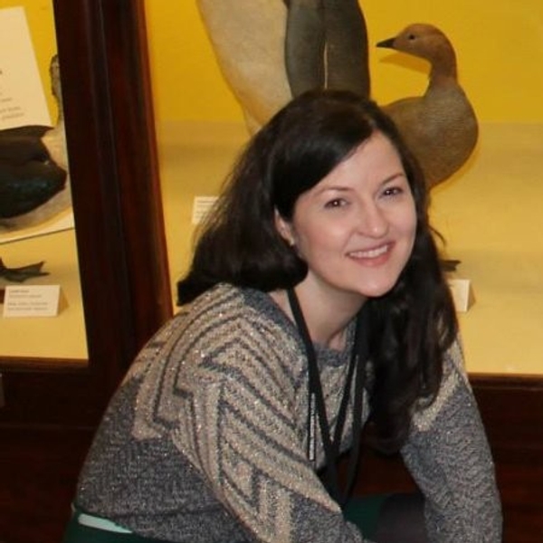 Smiling woman in a museum with bird exhibits in the background.