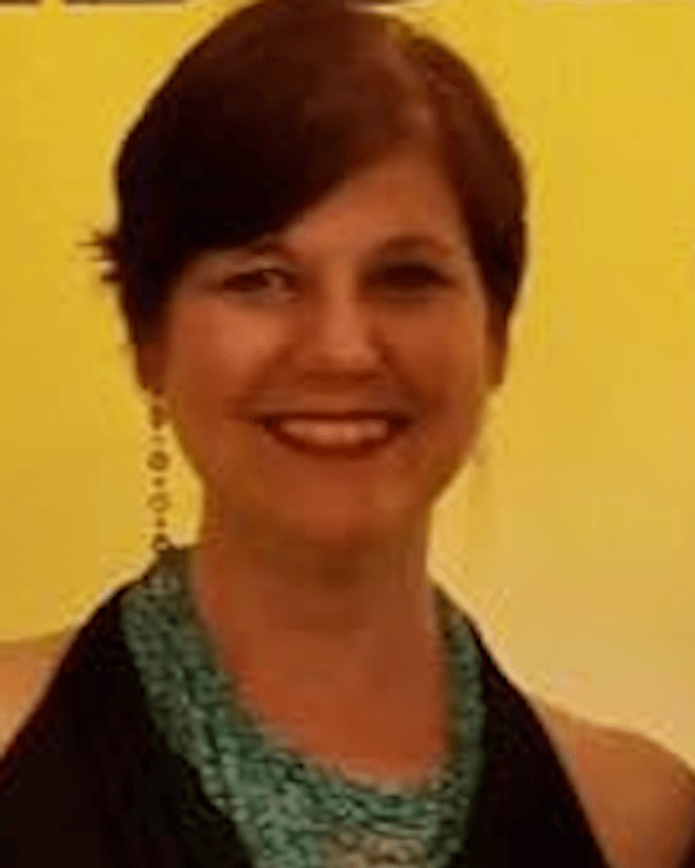 Smiling woman, Moira Conrad, with short dark hair, turquoise necklace against a yellow background.