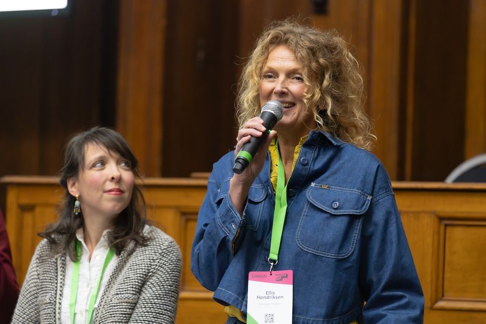 Smiling woman speaking into a microphone, another woman seated next to her, both wearing name tags.