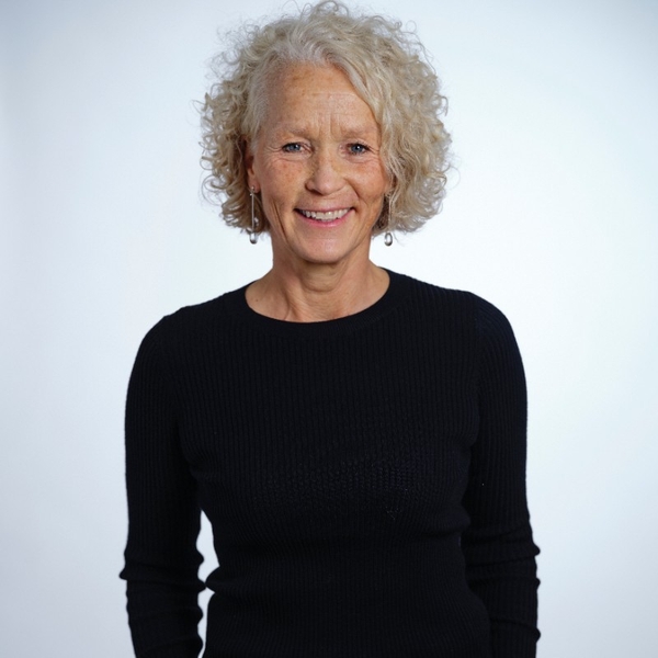 Smiling woman with curly gray hair in a black sweater against a light background.
