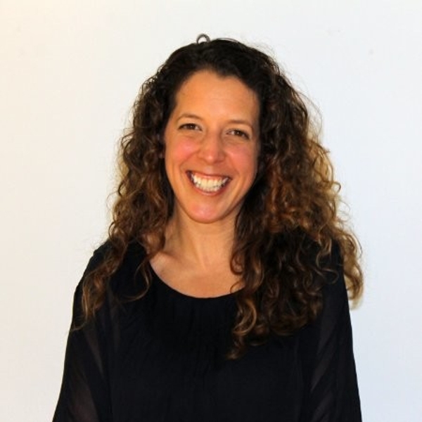 Smiling woman with curly hair wearing a black top against a plain background.