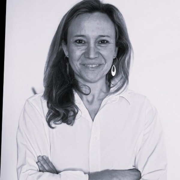 Smiling woman with long hair in a white shirt, arms crossed, against a light background.