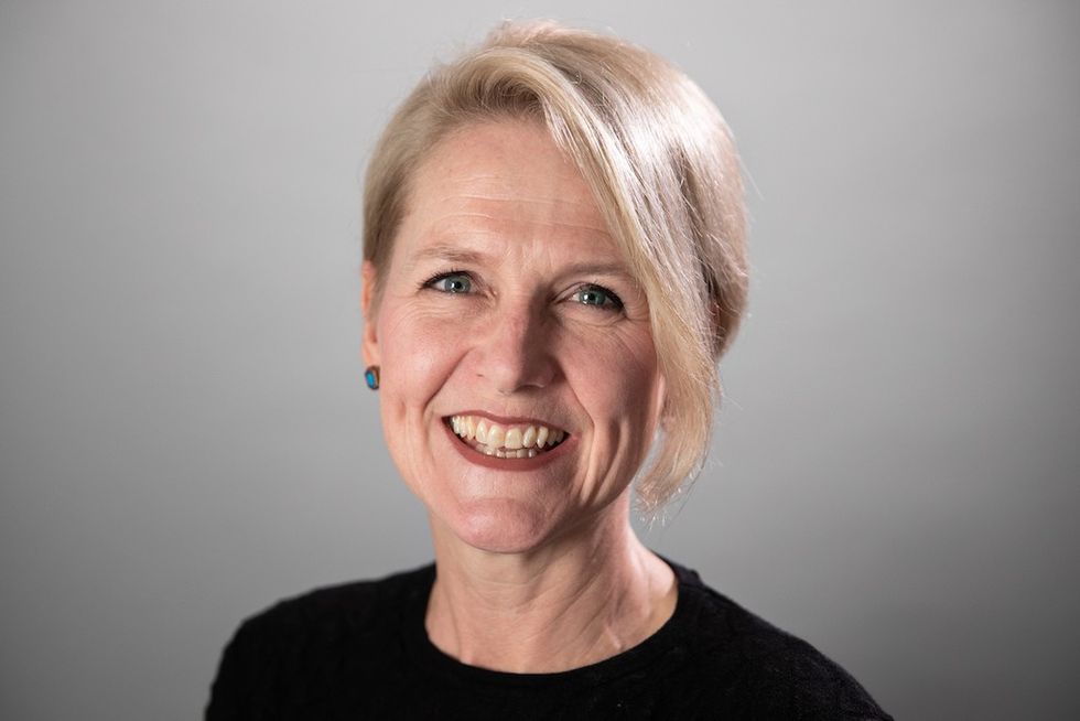 Smiling woman with short blonde hair, wearing a black top and blue earrings.