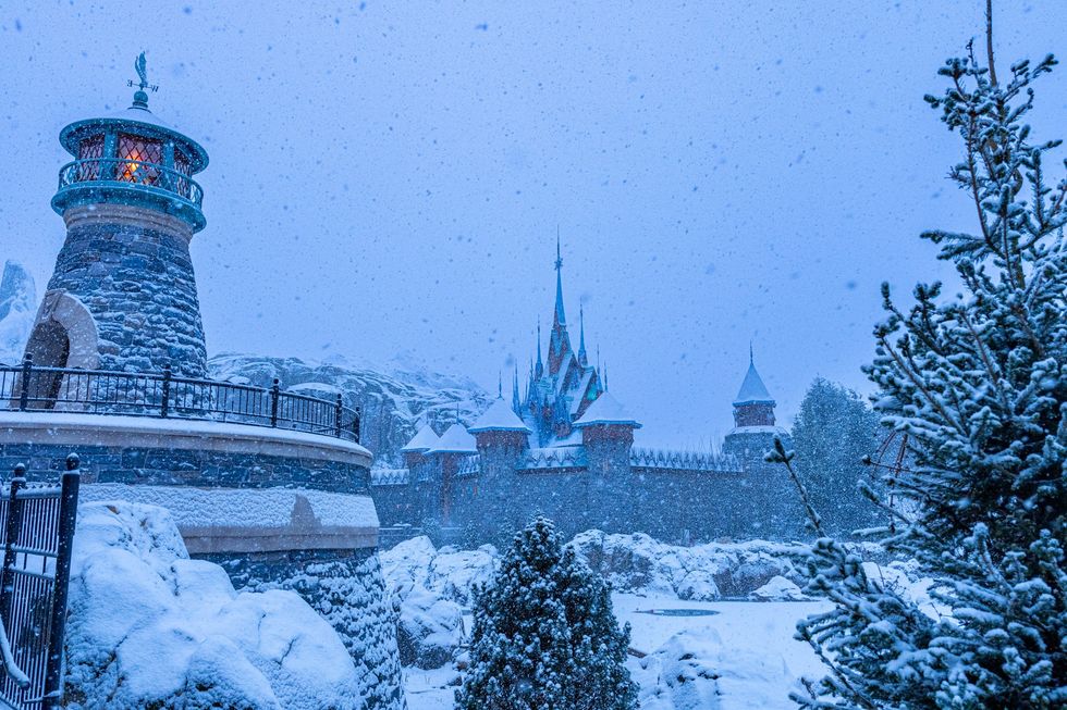 Snowy castle scene with a stone tower and trees, enveloped in falling snowflakes at Disneyland Paris