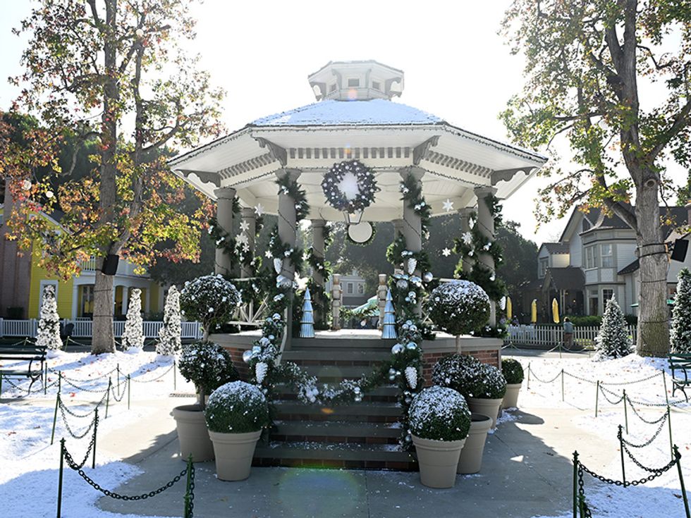 Snowy gazebo decorated for winter, surrounded by snowy trees and potted plants.