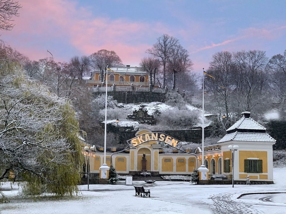 Snowy Skansen entrance with serene sunset sky and frosted trees.