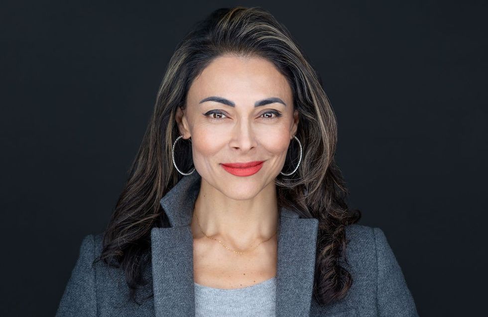 Sol Rashidi in gray blazer and hoop earrings against a dark background.
