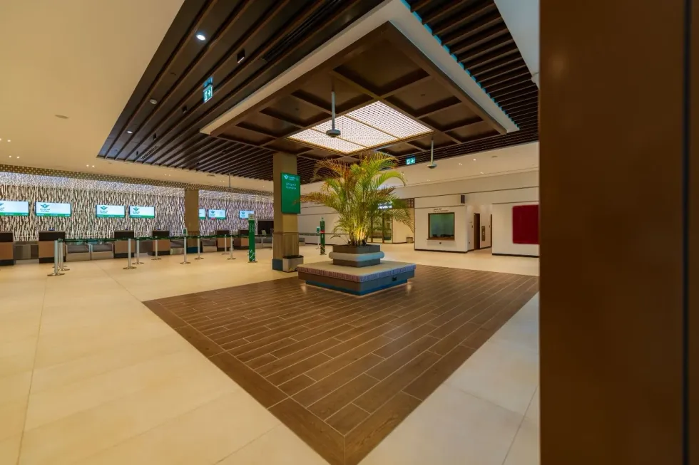 Spacious airport lobby in Saudi Arabia with a central plant and check-in counters.