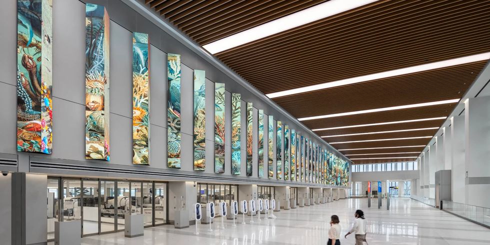 Spacious airport terminal with vibrant, vertical sea life murals above a security checkpoint.