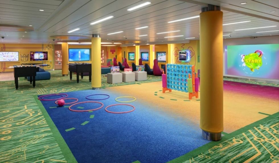 Spacious, colourful kids\u2019 playroom with games, screens, and seating areas on a cruise ship