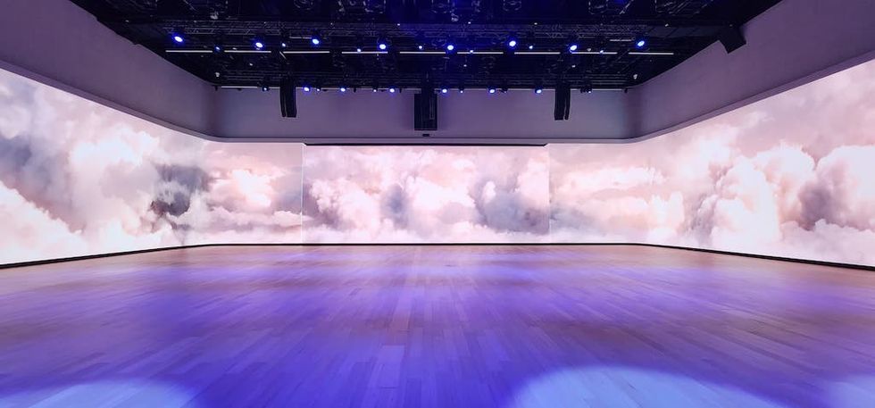 Spacious room with cloud-themed walls and a reflective wooden floor, lit by blue lighting.