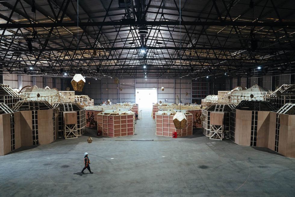 Spacious warehouse interior with large wooden geometric structures and a lone person walking.