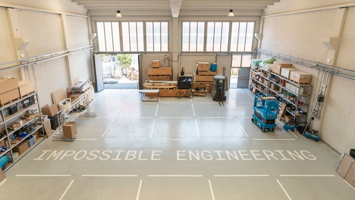 Spacious workshop at Leva Grid labelled "Impossible Engineering" with shelves and equipment.