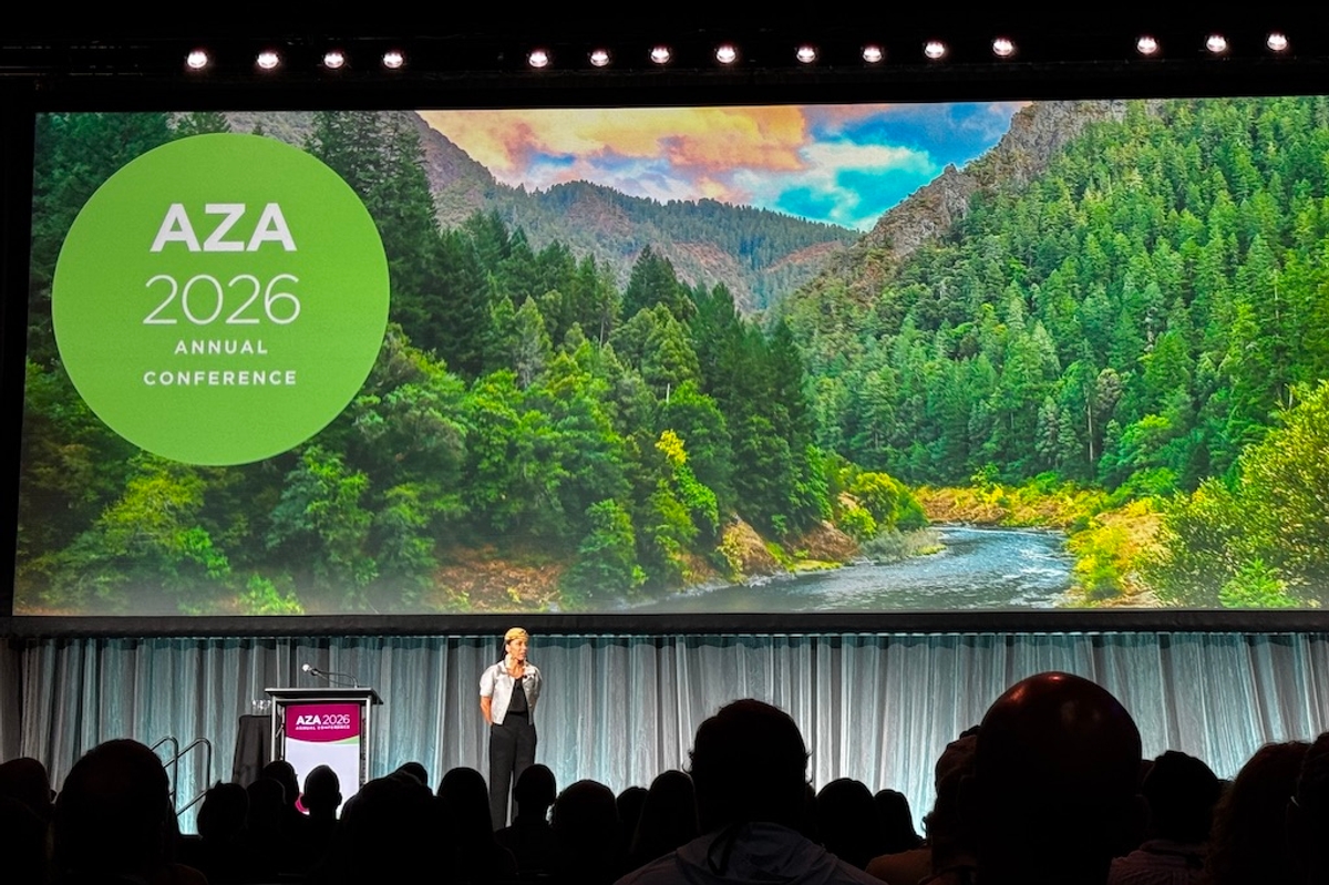 Speaker on stage at AZA 2026 conference with nature backdrop.