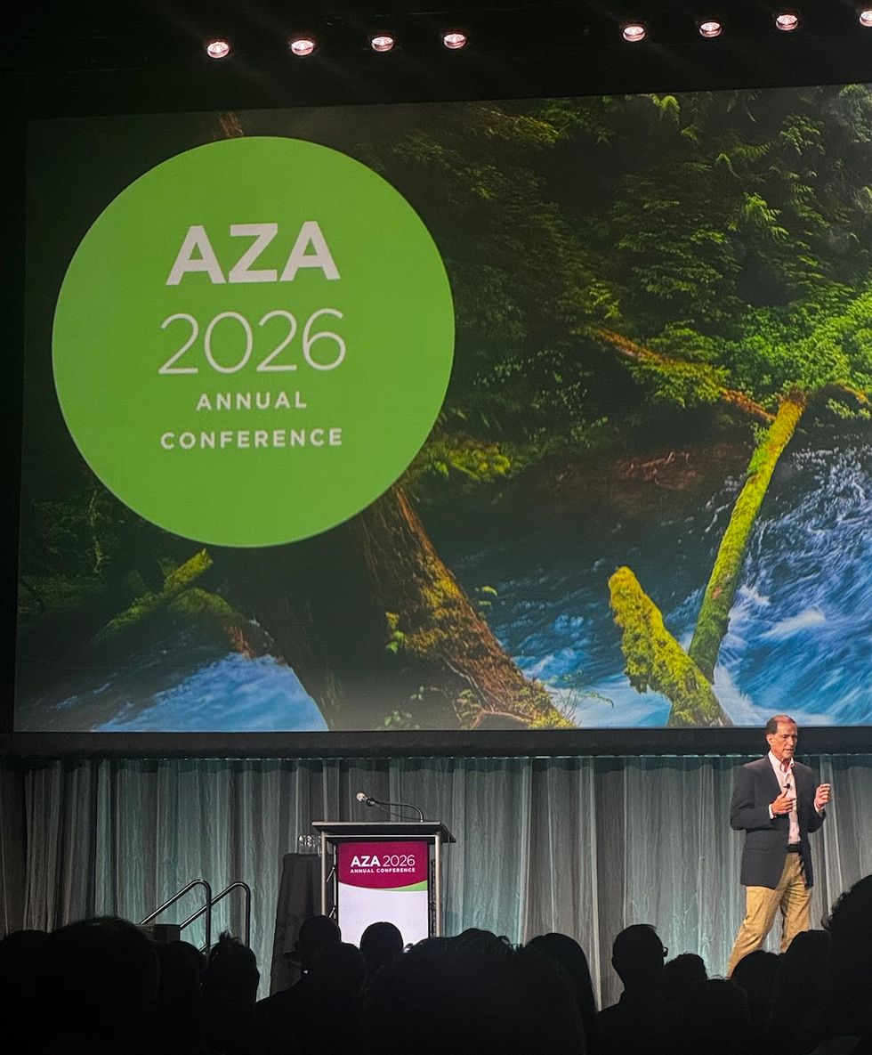 Speaker on stage at the AZA 2026 Annual Conference, large green logo projected.