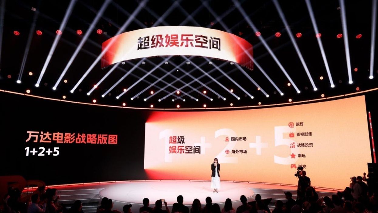 Speaker on stage with bright lights and screens displaying Chinese text and numbers.