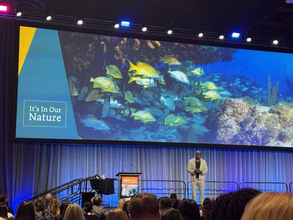 Speaker on stage with underwater scene and "It's In Our Nature" text on screen.