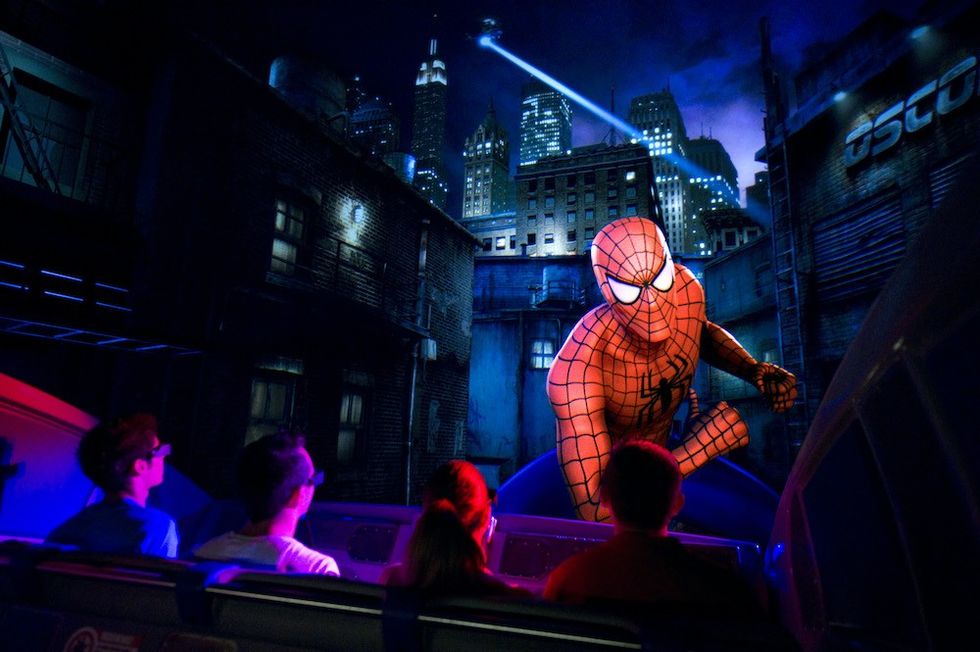 Spider-Man attraction with visitors, city skyline backdrop, nighttime setting.