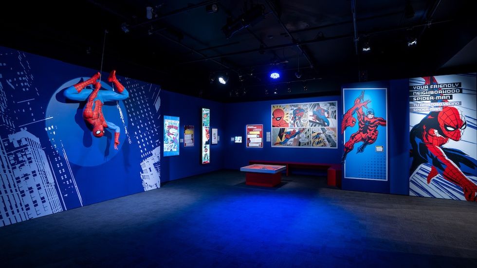 Spider-Man exhibit with artwork and hanging model in a blue-lit room.
