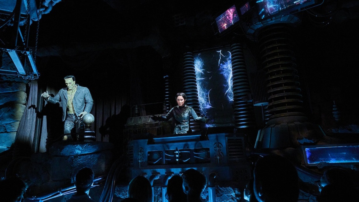 Spooky lab scene from Epic Universe's Monsters Unchained dark ride with Franekstein animatronic, control panel, and glowing electric effects; audience watches.