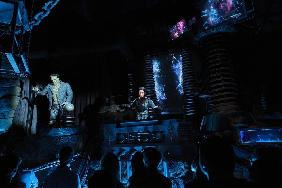 Spooky lab scene from Epic Universe's Monsters Unchained dark ride with Franekstein animatronic, control panel, and glowing electric effects; audience watches.