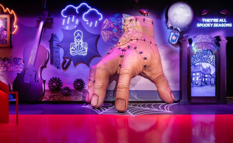 Spooky themed room with a giant hand, neon art, and "Nevermore Academy" gate at Netflix House