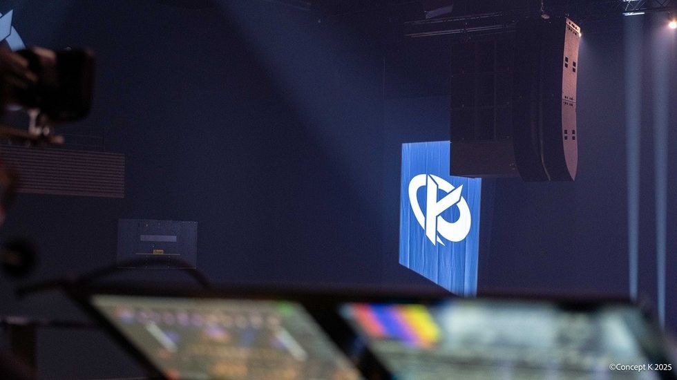 Stage with blue logo projection and blurred control panel in foreground.