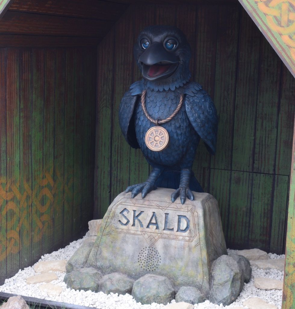 Statue of a blue raven named "SKALD" wearing a medallion, on a stone pedestal at Paultons Park