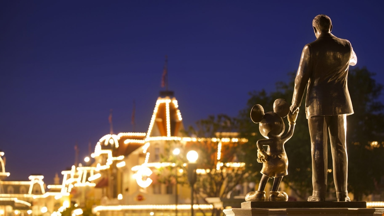 Statue of Walt Disney and Mickey Mouse at night, with illuminated buildings in the background.
