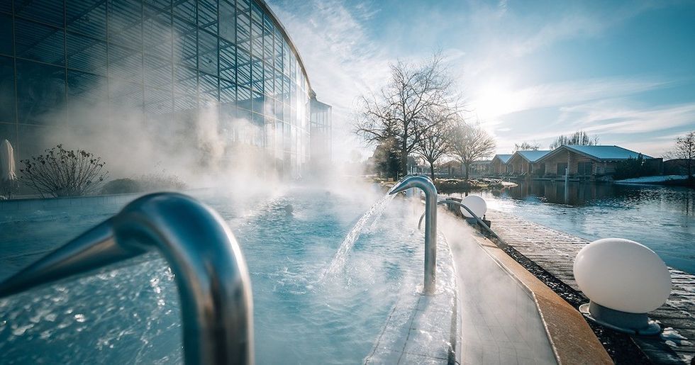 Steam rises from an outdoor pool near a glass building on a sunny day.