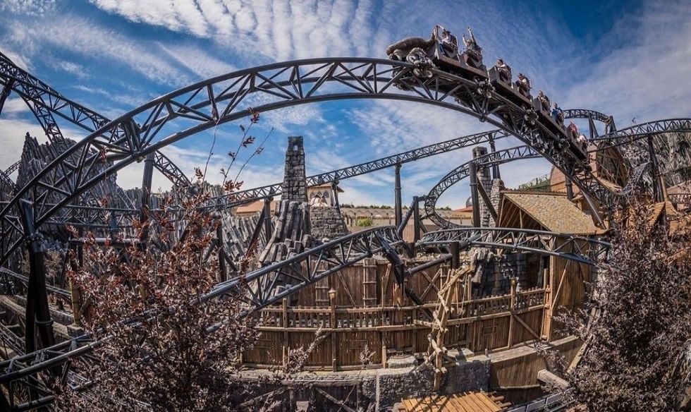Steel roller coaster twists through wooden structures under a cloudy sky, Phantasialand's Taron