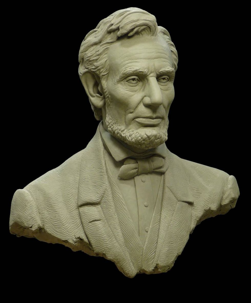 Stone bust of a bearded man in a suit and bow tie, on a black background.
