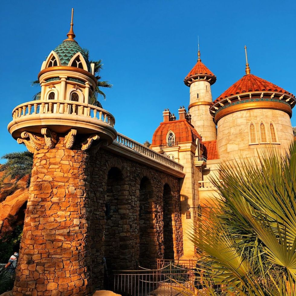 Stone castle with red rooftops against a clear blue sky.