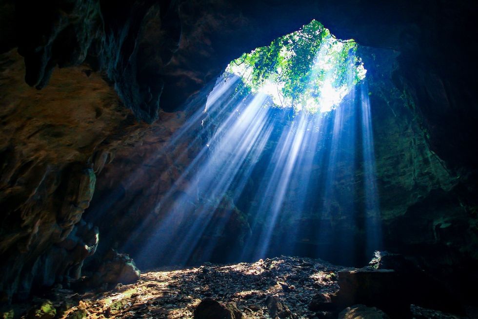 Sunlight streams through a hole in a cave ceiling, illuminating the rocky interior.