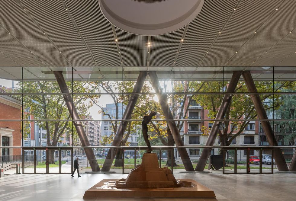 Sunlit atrium with a large window, sculpture, and person walking.