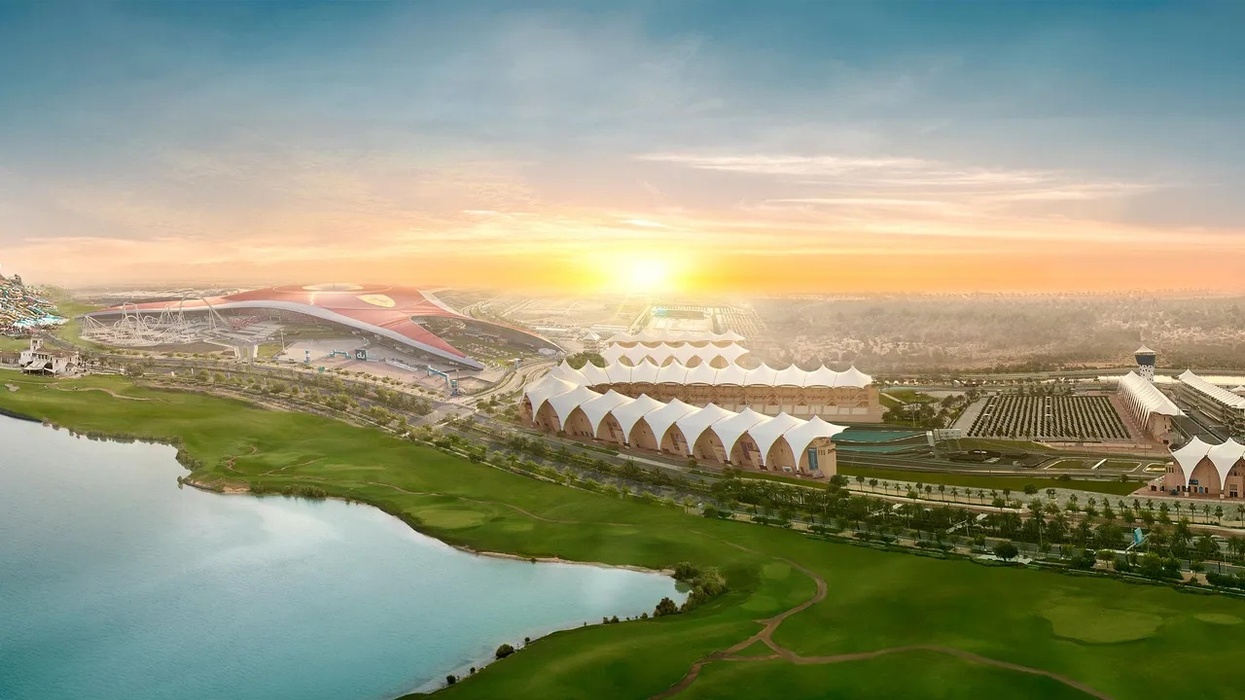 Sunlit landscape called Yas Island with futuristic buildings, greenery, and a lake under a vast sky.