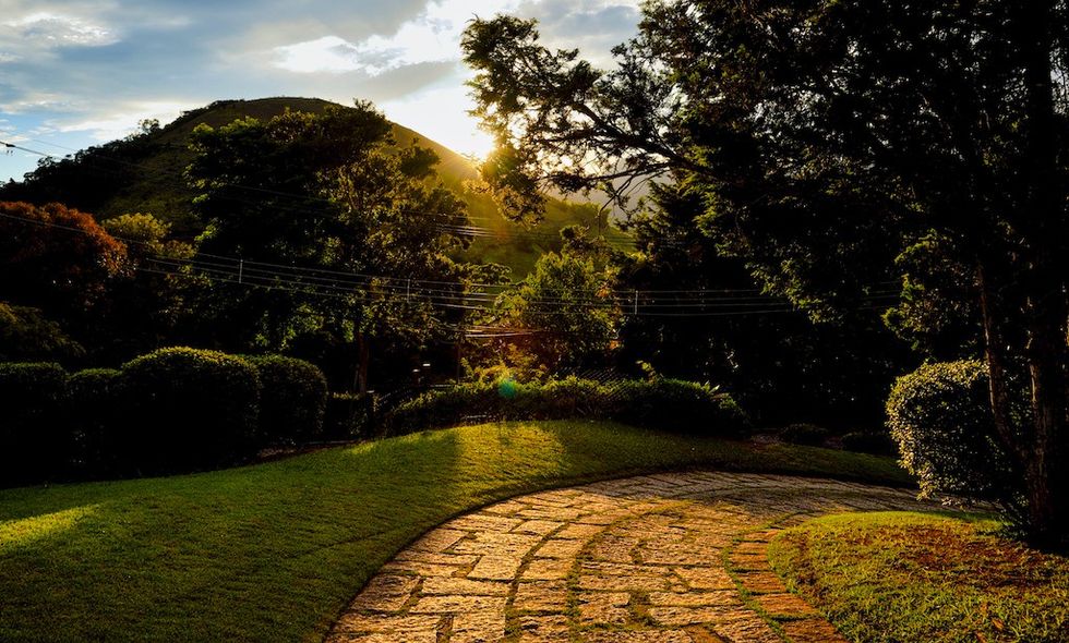 Sunset over a hilly landscape with trees and a stone pathway.