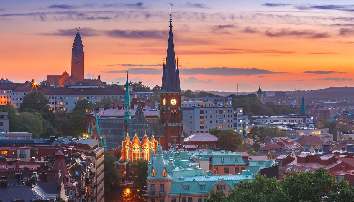 Sunset over Gothenburg cityscape with illuminated church spires and colorful buildings.