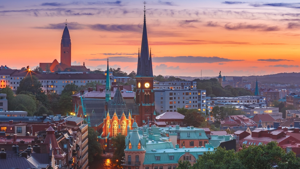 Sunset over Gothenburg cityscape with illuminated church spires and colorful buildings.