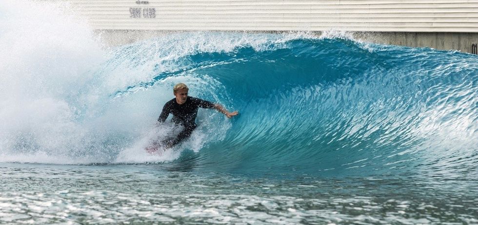 Surfer riding a blue wave inside a wave pool.